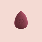 A Aspilon Cosmetics teardrop-shaped makeup sponge in a burgundy color centered on a solid pale pink background.